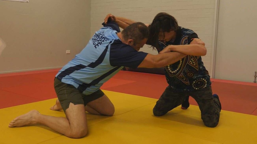 A man wrestles with a teenage boy on a red and yellow mat.