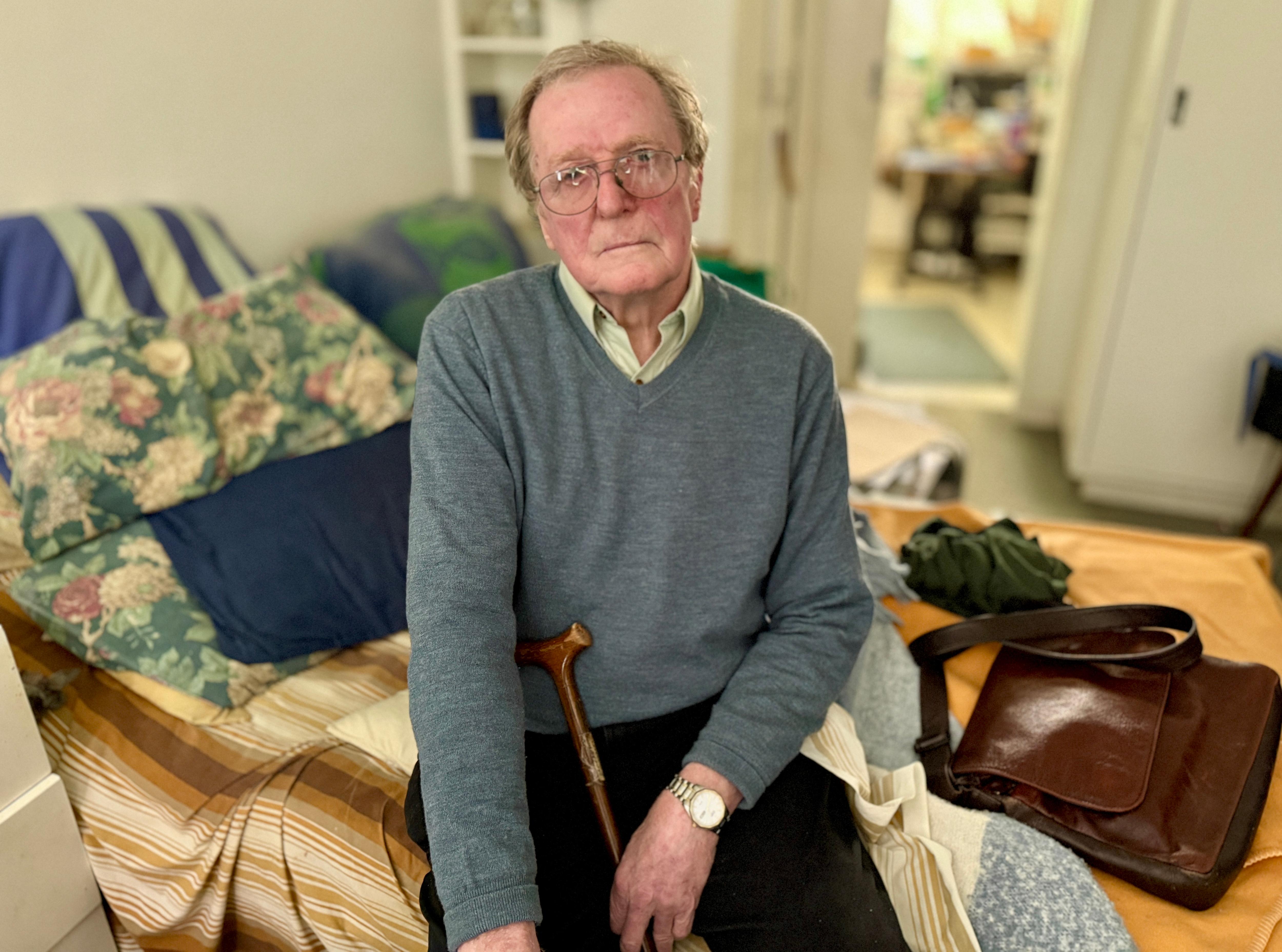 David Phillips se sienta en su habitación y mira a la cámara con expresión seria.