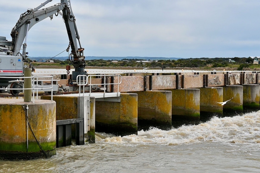 A crane on the top of the Goolwa barrages, as water flows underneath.