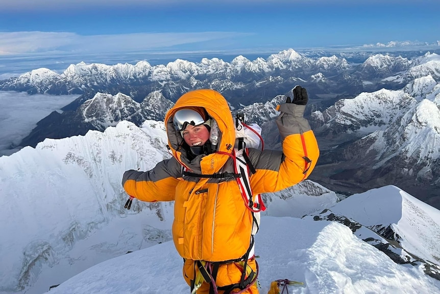 Gabby Kanizay célèbre au sommet du mont Everest, avec des rangées de sommets enneigés en arrière-plan.
