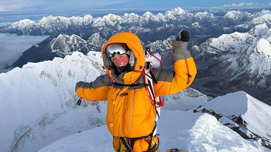 Gabby Kanizay celebrates on the summit of Mount Everest, with rows of snow-capped peaks in the background.