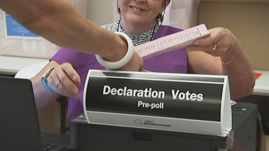 An election official hands a pre-poll voting form to a voter