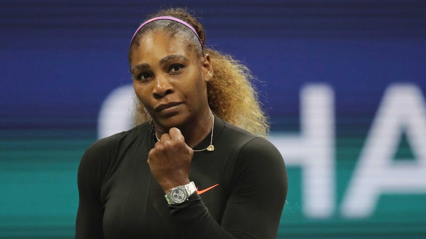 Serena Williams clenches her fist while wearing a dark, long sleeved top and silver watch