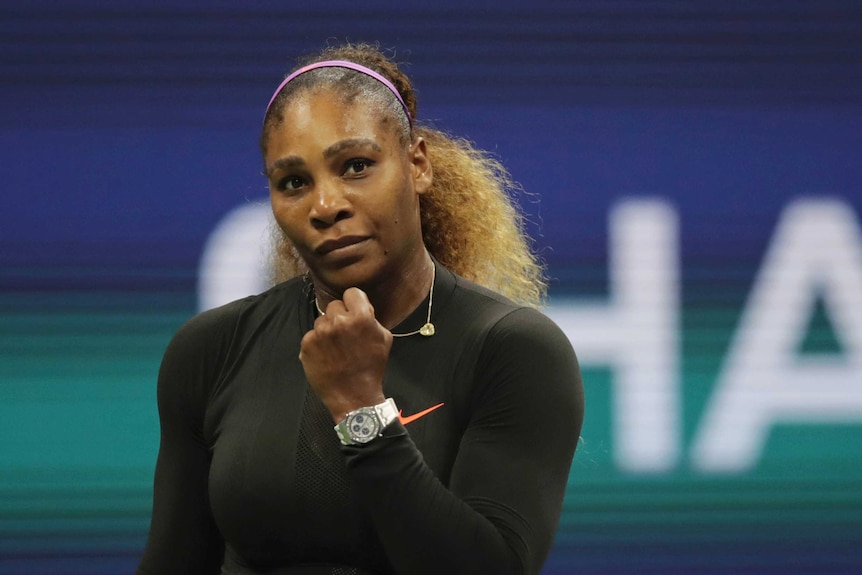 Serena Williams clenches her fist while wearing a dark, long sleeved top and silver watch