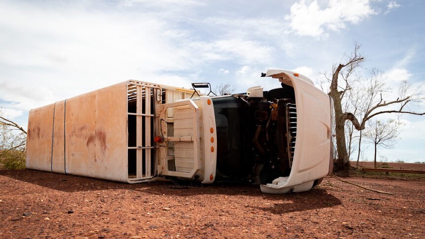 A semi-trailer lies on its side in red dirt