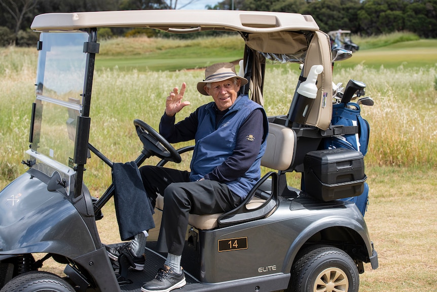 An elderly man smiles from inside a golf buggy