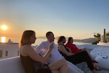 Jessica Wong and her friends sit on a rooftop in Mykonos with the sun setting over the Mediterranean.