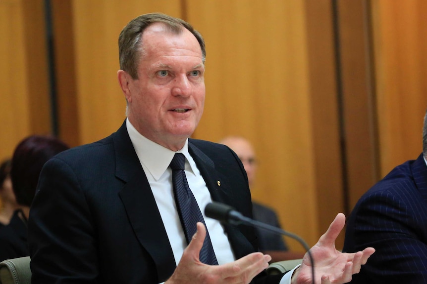 Chris Jordan, his hands outstretched in an explanatory manner, speaks into a microphone