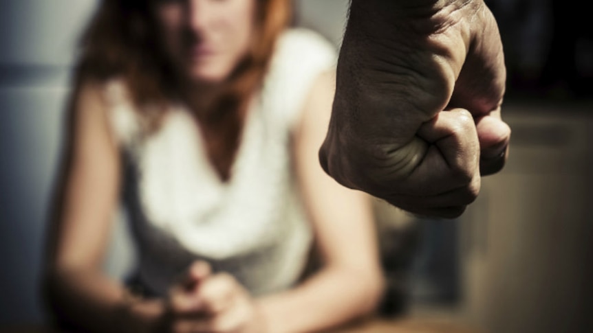 A man's fist in the foreground with cowering woman out of focus.