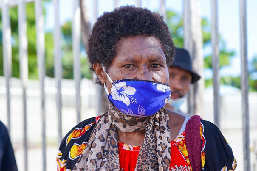 A Papua New Guinean woman in a bright dress and tropical print face mask