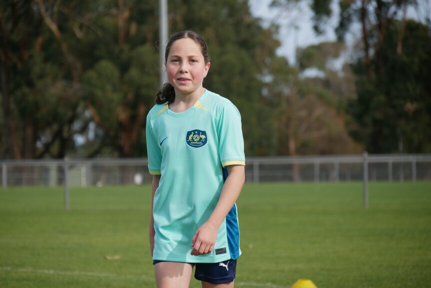 A girl wearing an Australia soccer shirt standing out on a field. 