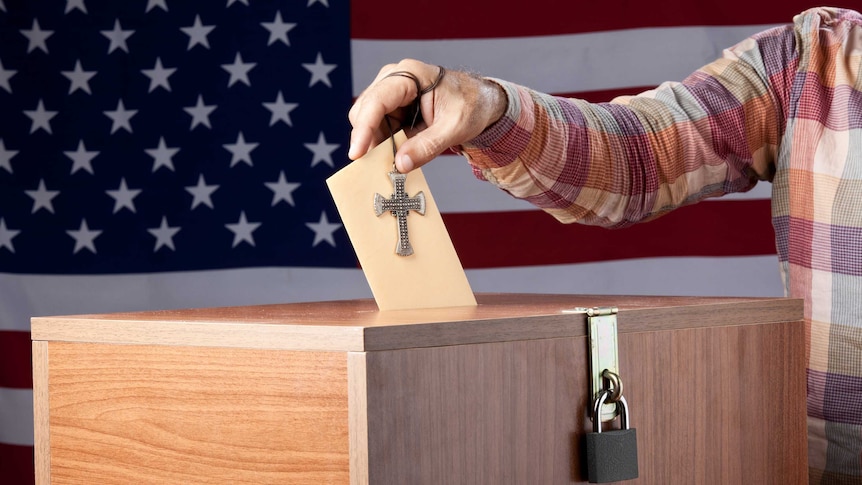 Man putting envelope into ballot box in front of the American flag.