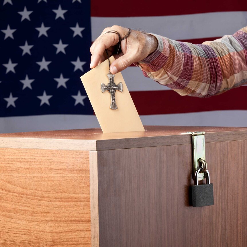 Man putting envelope into ballot box in front of the American flag.