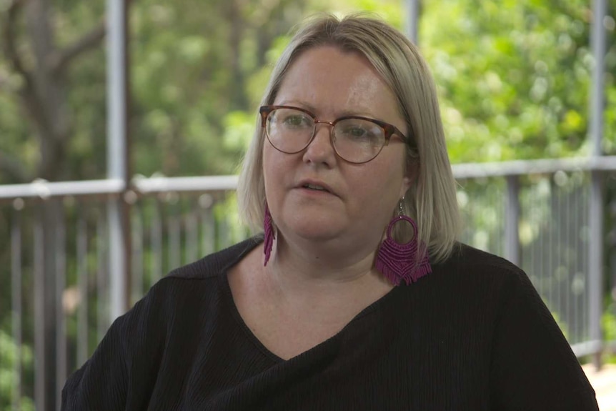 A blonde woman wearing a black shirt and purple earrings with glasses.