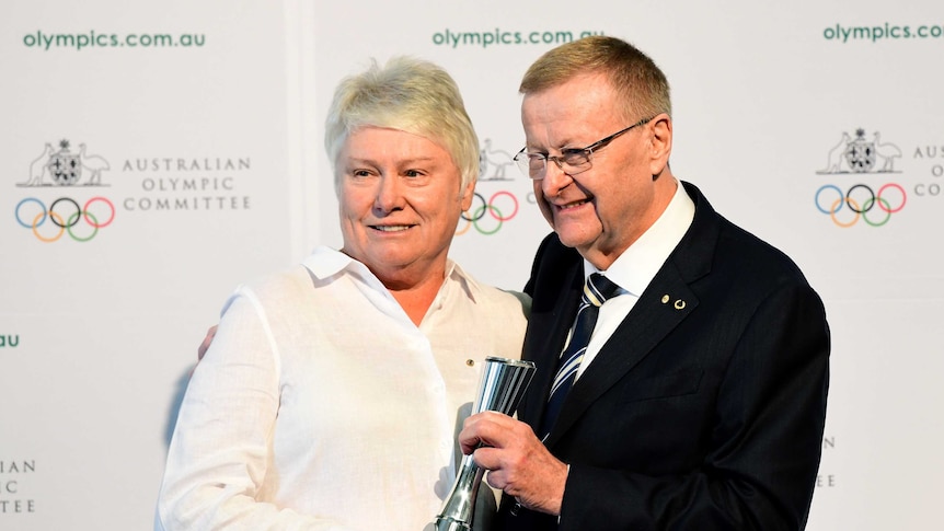 A woman and a man holding a statue with the words Australian Olympic Committee on the wall behind them.