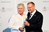 A woman and a man holding a statue with the words Australian Olympic Committee on the wall behind them.
