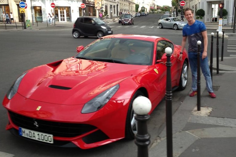 George Moore wearing jeans and a t-shirt photographed next to a red Ferrari.