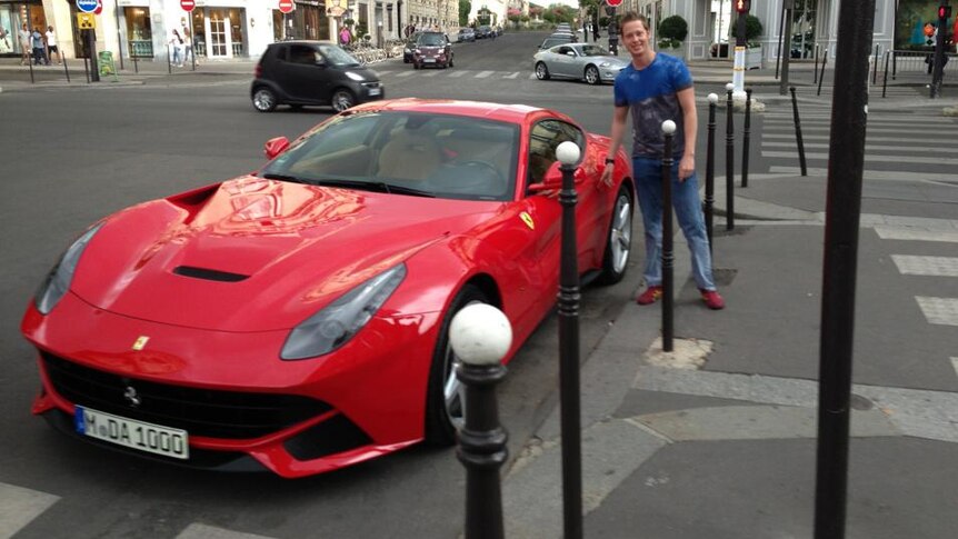 George Moore wearing jeans and a t-shirt photographed next to a red Ferrari.