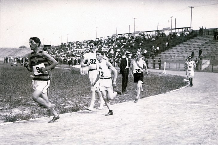 A black and white photo of men running a marathon around an open stadium