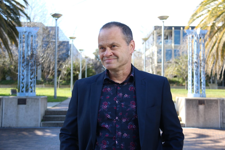 A man wearing a navy blazer and shirt smiling outdoors in Canberra