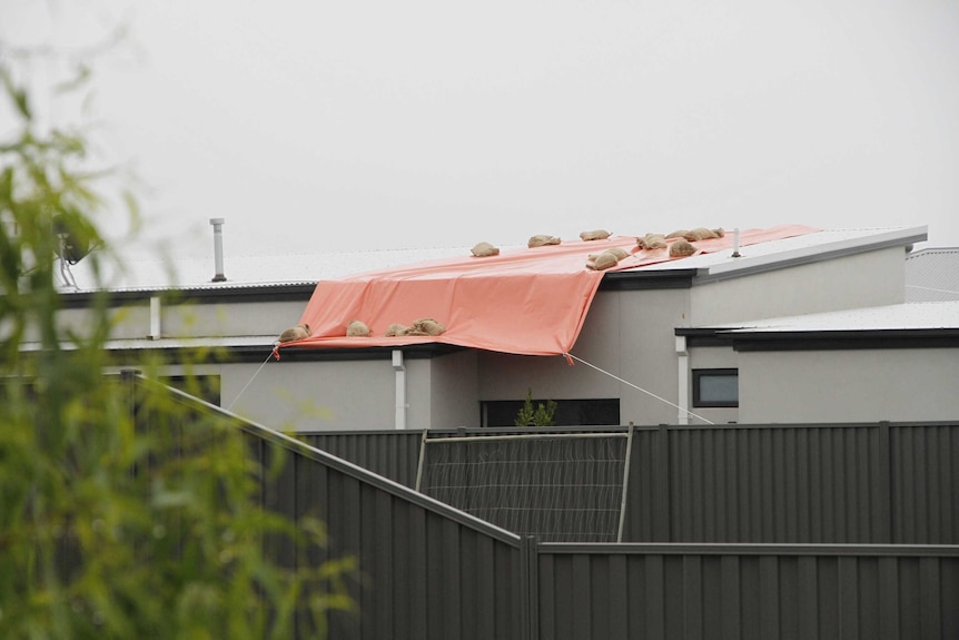 A damaged roof covered with an orange tarp.