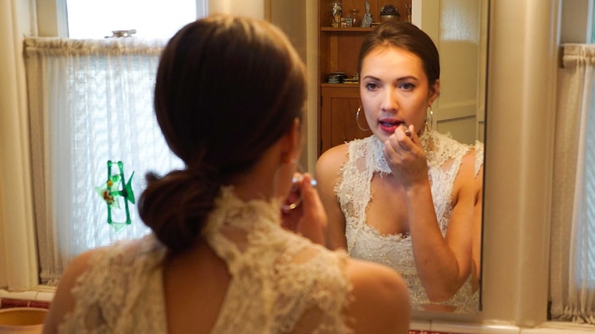 Emily Coupe applies lipstick in a bathroom