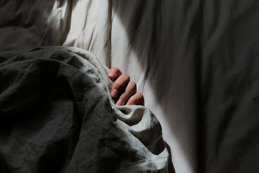 A woman's hand can be seen among bed sheets