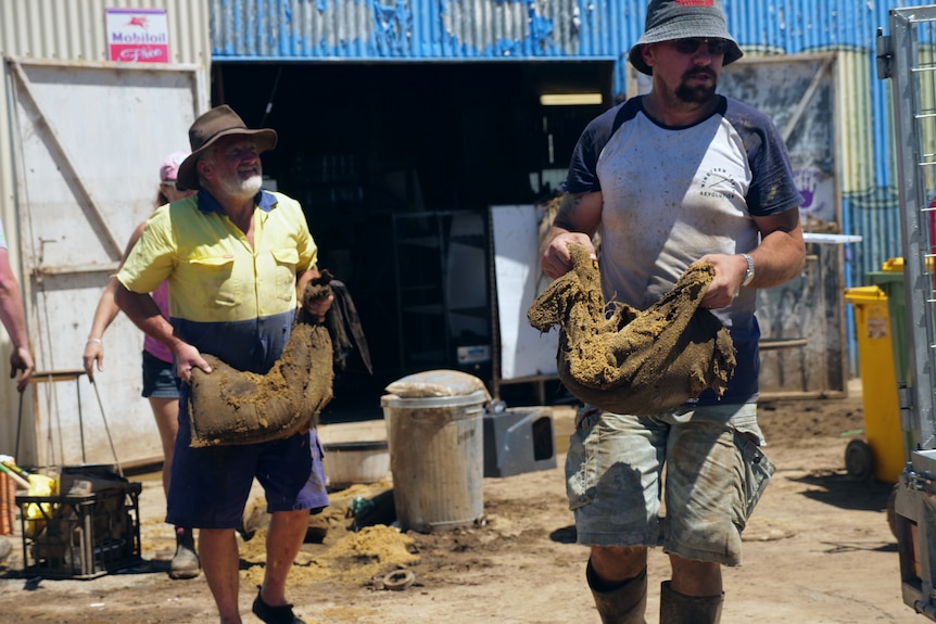 Two men hold sandbags in their hands and work.