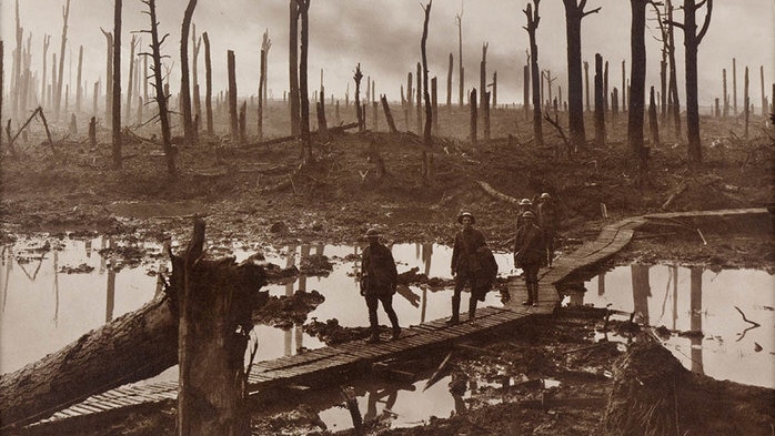 Soldiers walk across a wooden boardwalk through a destroyed landscape