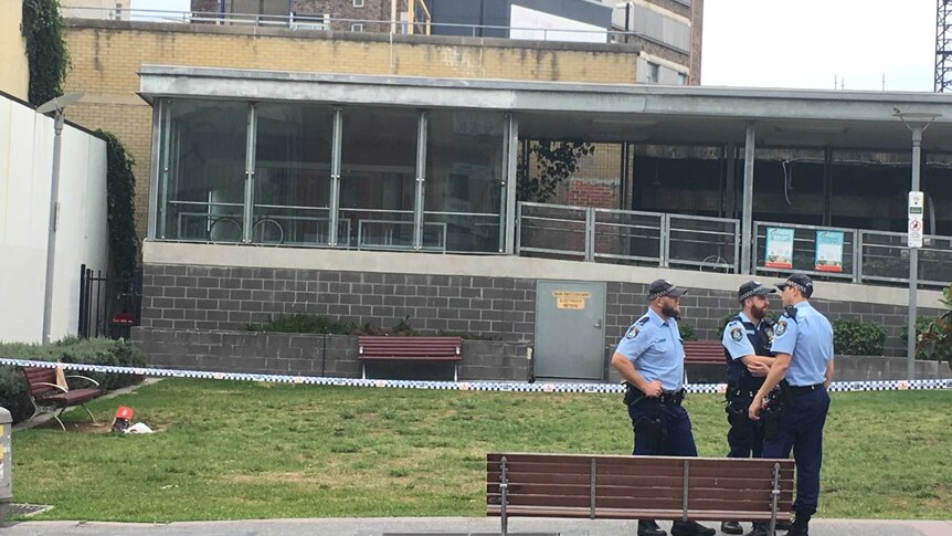 Police and police tape near a grassed area outside Hurstville train station.