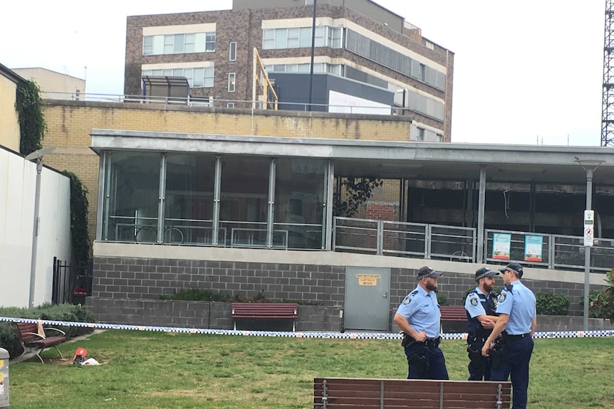 Police and police tape near a grassed area outside Hurstville train station.