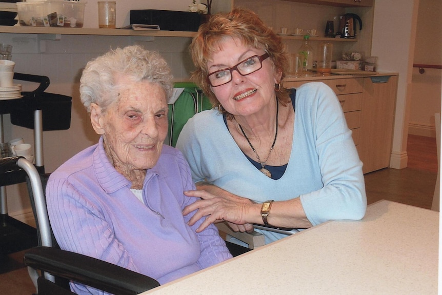 Leonora smiles, sitting next to her elderly mother who is in a wheelchair.