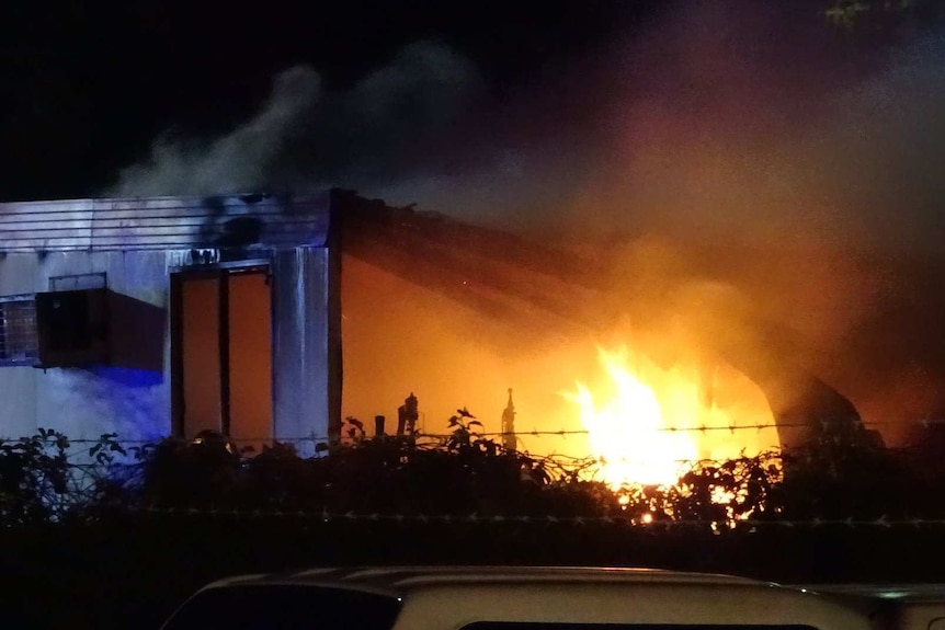 Flames and smoke leap from a demountable building at night.