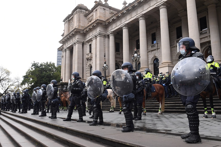 Riot police in helmets and shields stand in front of mounted officer on horseback on the steps of Parliament House.