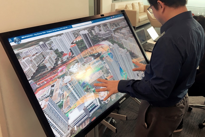 A man stands in front of a screen showing a 3d model of Singapore. 