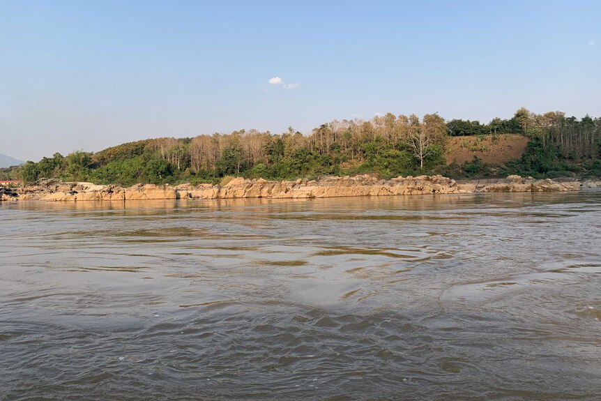 Rocks can be seen along the edge of the Mekong River, the photo is taken from a boat.
