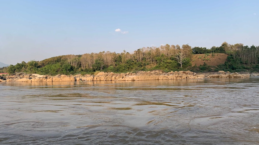 Rocks can be seen along the edge of the Mekong River, the photo is taken from a boat.