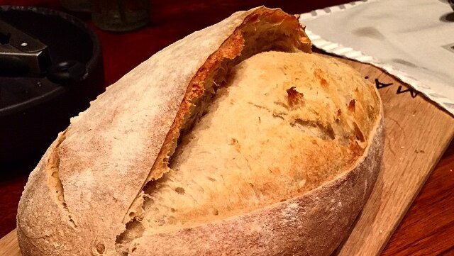 A baked loaf of sourdough bread on a wooden chopping board.
