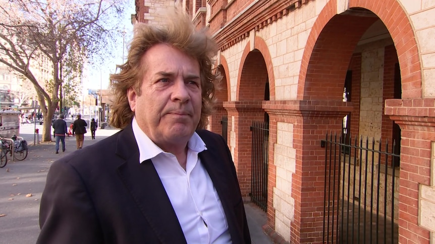 A man with long light brown hair outside an old building