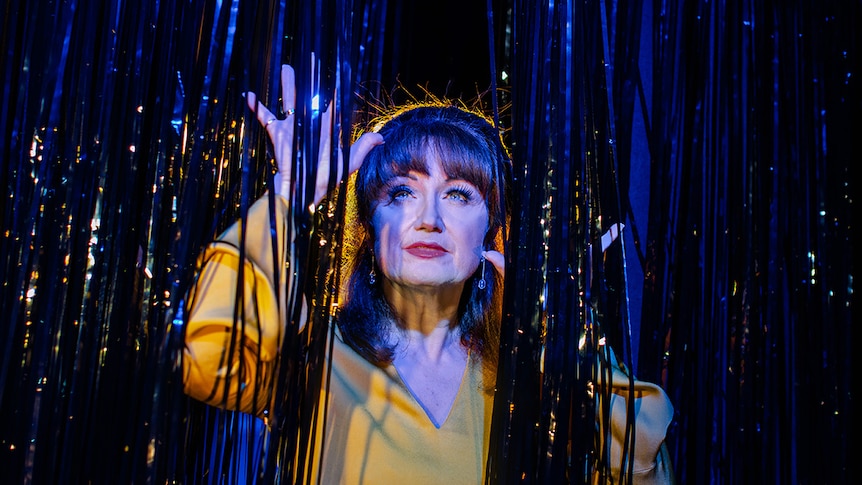 Colour photo of musical theatre actor Caroline O'Connor looking up and through tinsel curtain.