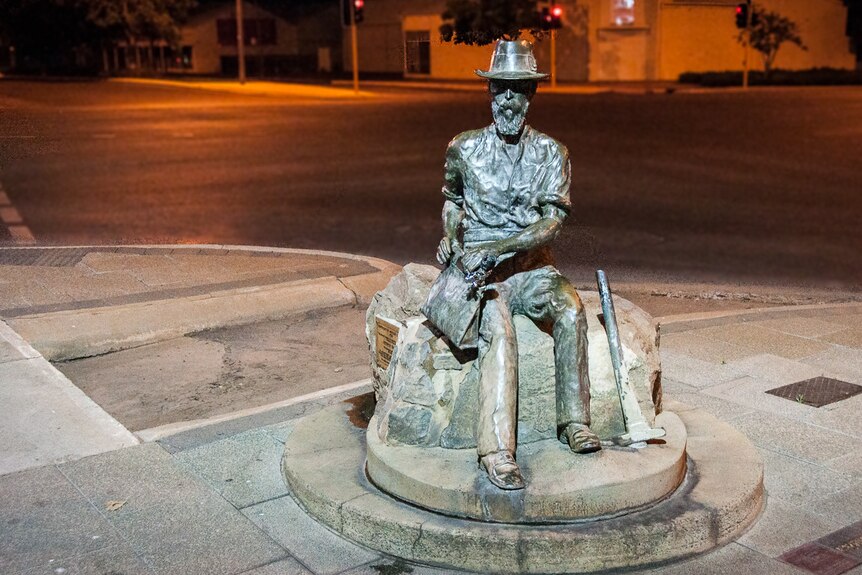 A bronze statue of a man sitting down, wearing a hat.