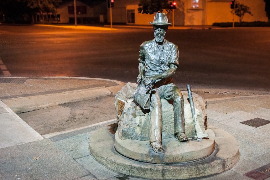 A bronze statue of a man sitting down, wearing a hat.