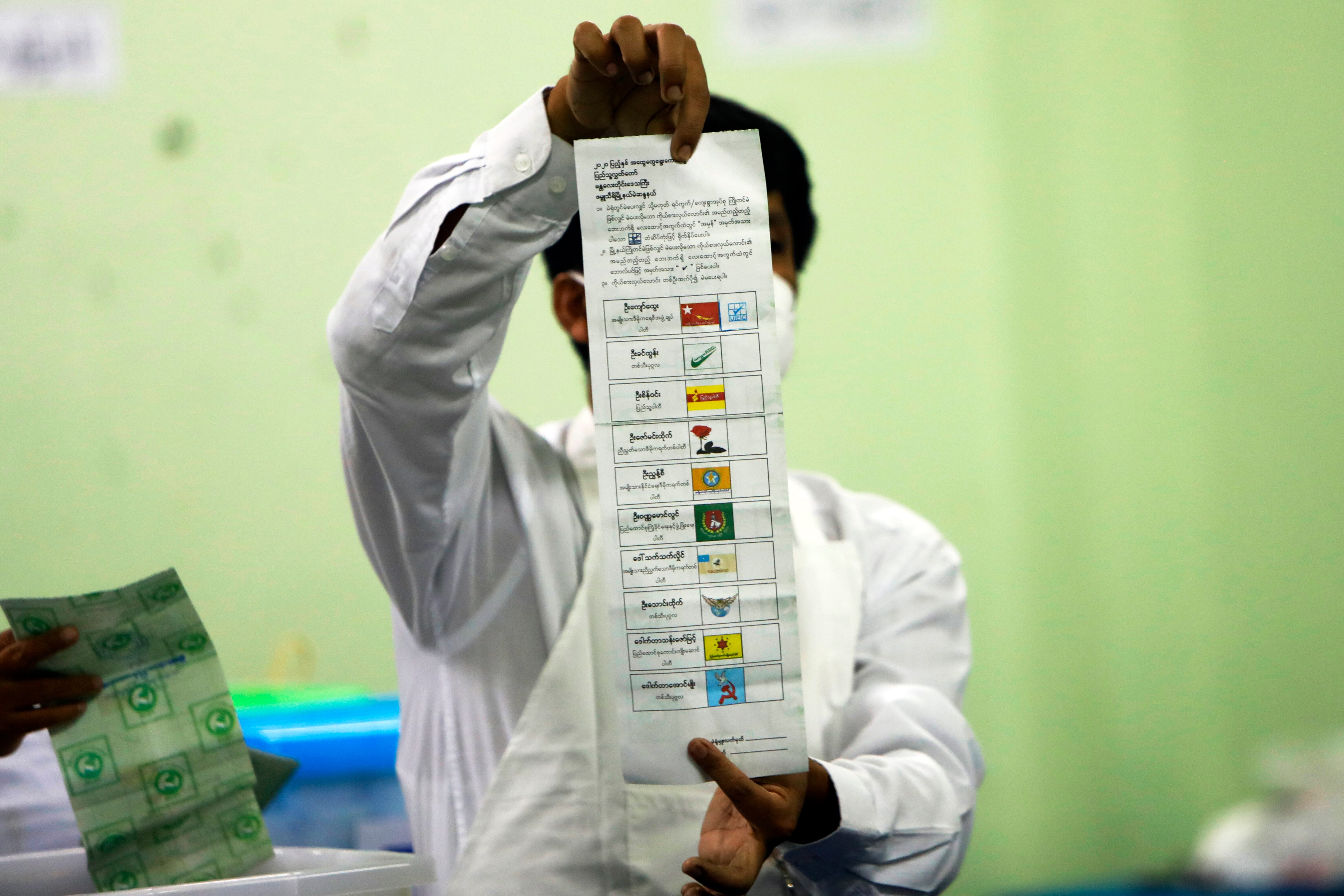 An official holds a long ballot paper aloft and counts the results makred in boxes next to coloured political party logos.