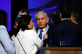 Israeli Prime Minister Benjamin Netanyahu looks past the camera in a crowd of people onstage in front of a blue background.