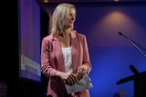 Rebecca White in a pink suit stands on stage in front of the tally room, clutching notes.