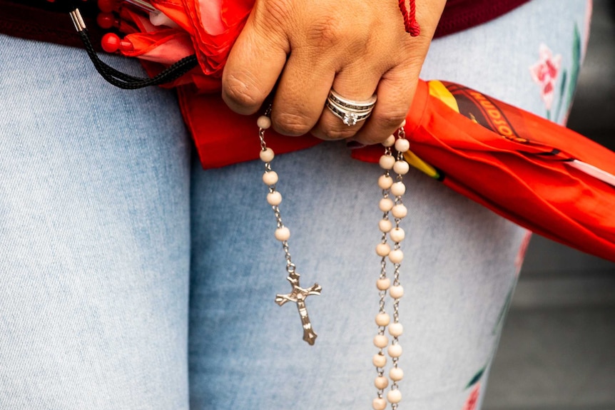 A close up of a woman clutching rosary beads