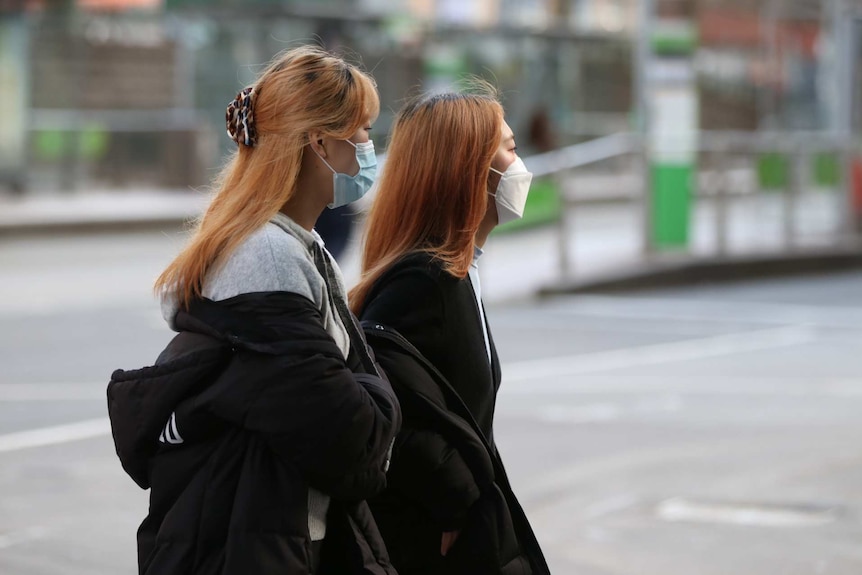 Two women in masks walking near a tram stop in Melbourne