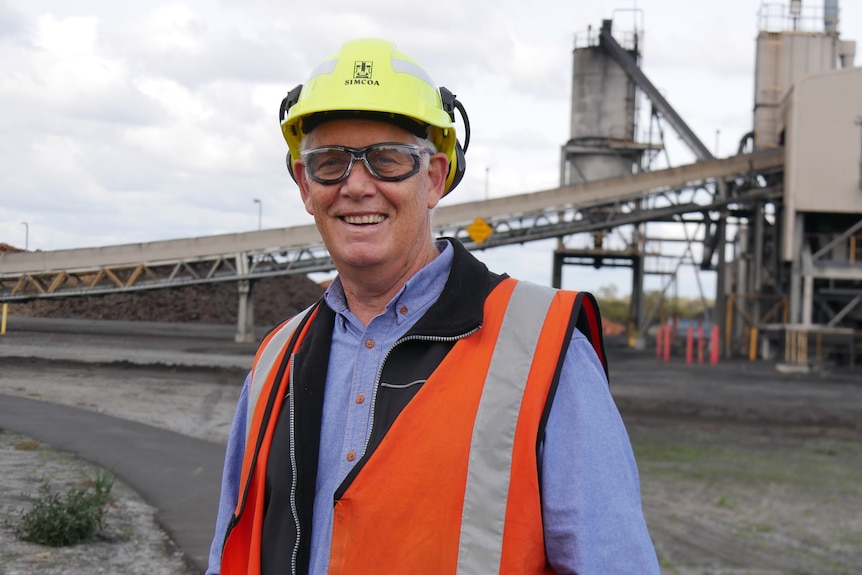 Production director standing in front of a silica processing plant, wearing helmet, goggles and high visibility mirror.