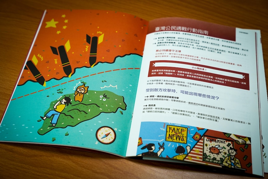 A booklet open on a table shows an illustration of Taiwan with cartoon people cowering below Chinese missiles