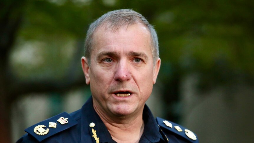 Michael Outram wears a blue police-styled uniform as he addresses the media in a courtyard